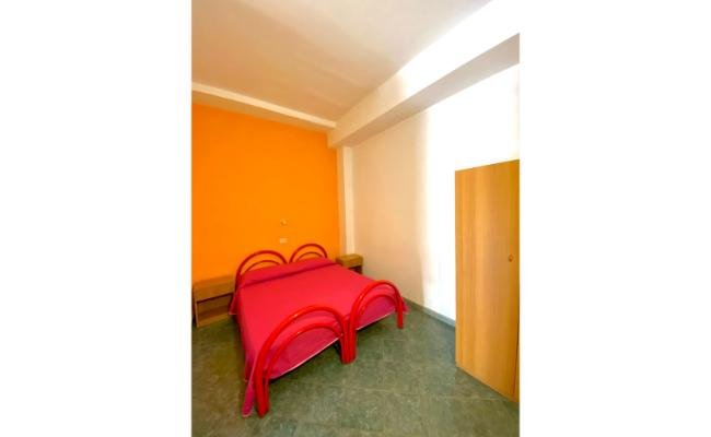 Camera da letto con pareti arancioni, letto matrimoniale rosso e armadio a destra.