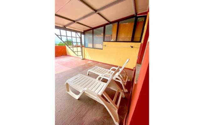 Terrazza coperta con due lettini bianchi e pavimento rosso.