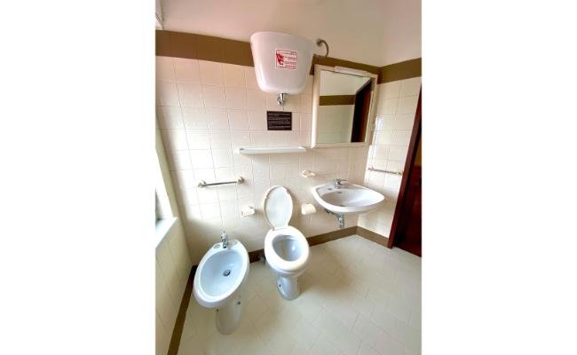 Bagno con bidet, water, lavabo e specchio. Piastrelle beige e cisterna in alto.