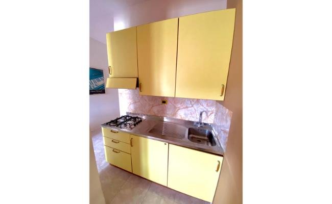Cucina con mobili gialli, piano cottura, lavabo e rivestimento in marmo.