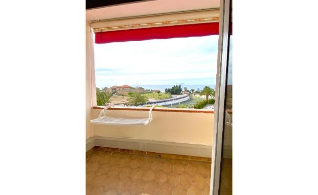 Balcone con vista mare, tettoie rosse e sedile appeso al muro.