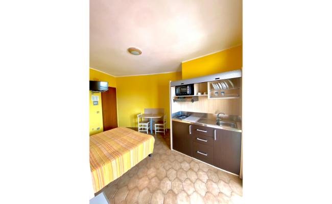 Camera con letto matrimoniale, cucina compatta e pareti gialle.