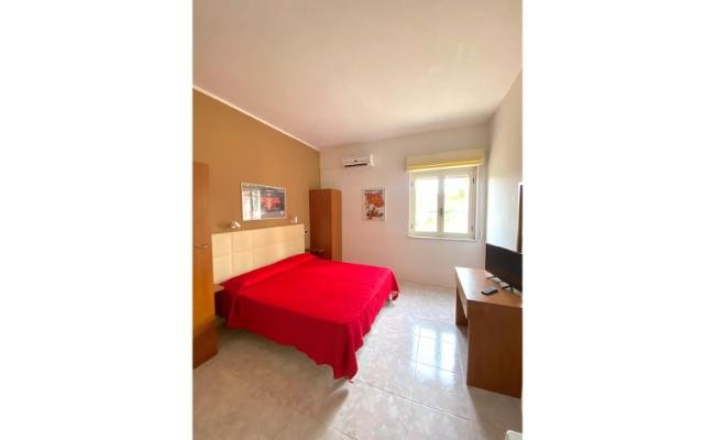 Stanza luminosa con letto matrimoniale e copriletto rosso, finestra e TV.