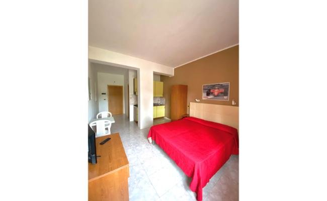 Camera da letto con letto matrimoniale, copriletto rosso, scrivania e TV.