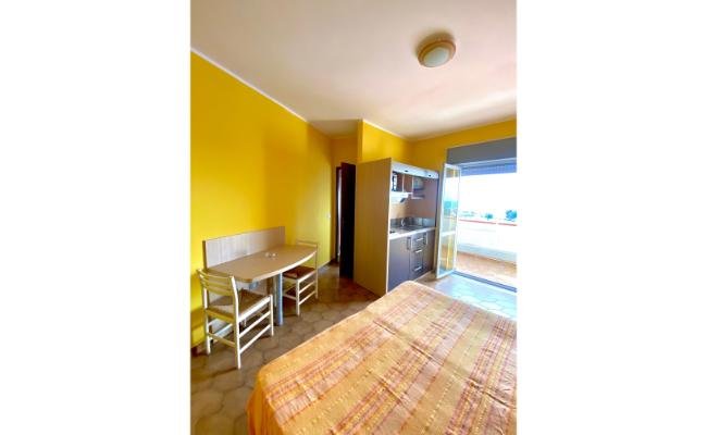 Camera con pareti gialle, letto, tavolo con sedie e accesso a un terrazzo.
