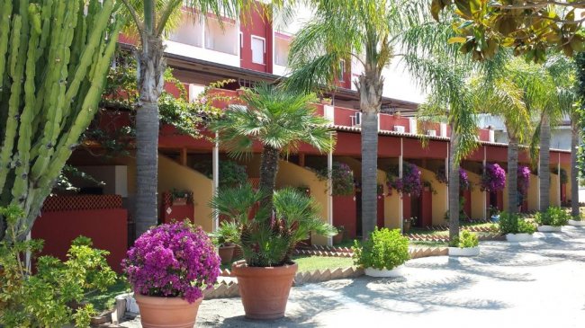 Un complesso residenziale con palme e vasi di fiori colorati lungo un viale soleggiato.