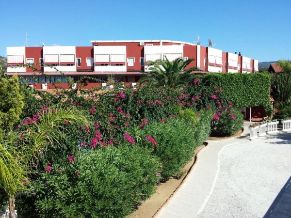 Un vialetto costeggiato da fiori e cespugli fioriti con un edificio rosso sullo sfondo.