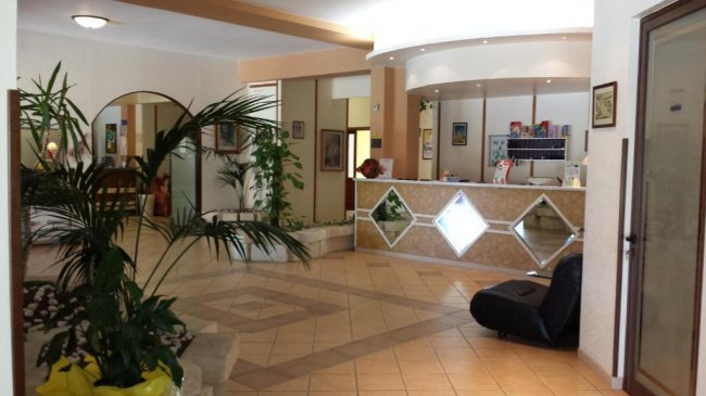 Una hall con pavimento piastrellato, piante e un banco reception decorato con specchi.