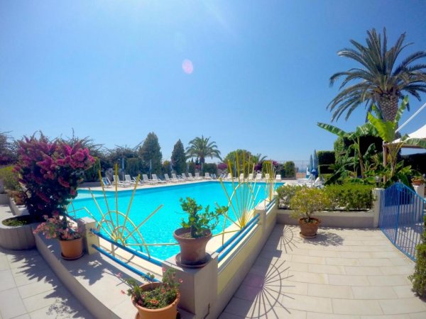 Piscina luminosa con fiori, piante e ampio cielo blu sullo sfondo.