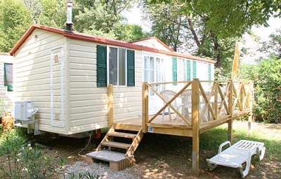 Una casa mobile con terrazza in legno e lettini, circondata da alberi.