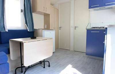 Interno di una casa mobile con tavolo pieghevole, divano blu e angolo cottura blu.