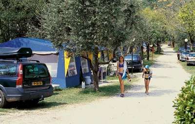Due persone camminano lungo un sentiero in un campeggio con tende e auto parcheggiate.