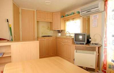 Piccola cucina con mobili in legno, televisore e aria condizionata.