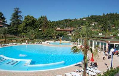 Piscina tonda con una piccola fontana, circondata da lettini e vegetazione lussureggiante.
