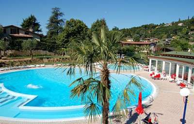 Piscina rotonda con palme, lettini e un'area relax, immersa in un paesaggio verdeggiante.