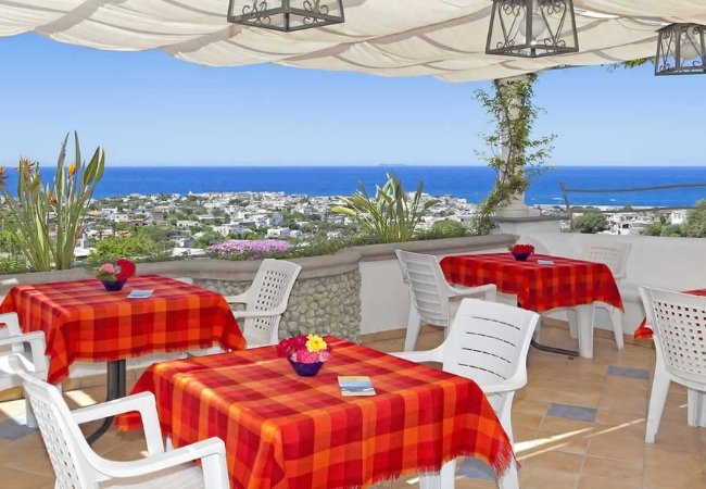 Terrazza coperta con vista sul mare e tavoli apparecchiati con tovaglie a quadri rossi.