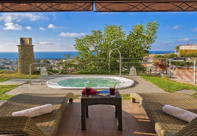 Due lettini e tavolino con vista su una jacuzzi e il mare.