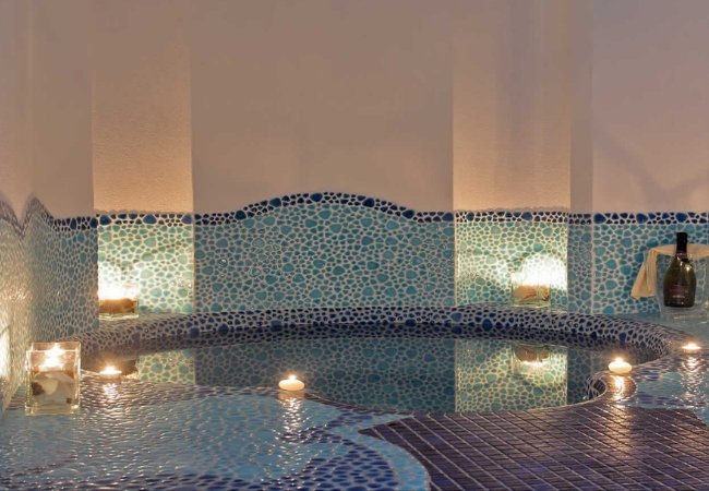 Vasca con mosaici blu, circondata da candele accese.