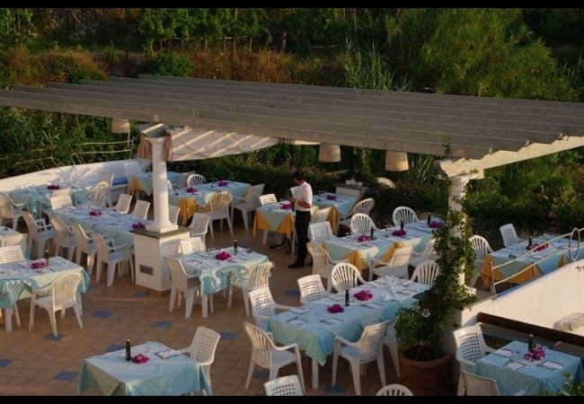 Ristorante all'aperto con tavoli apparecchiati sotto un pergolato.