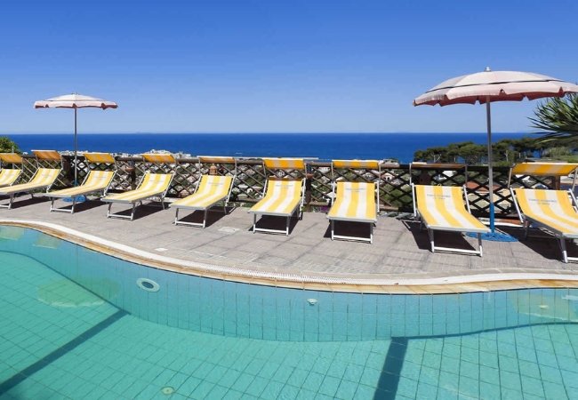 Lettini gialli e ombrelloni accanto a una piscina con vista sul mare.