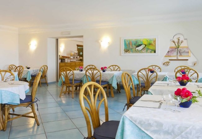 Sala da pranzo con tavoli apparecchiati e sedie in legno chiaro.