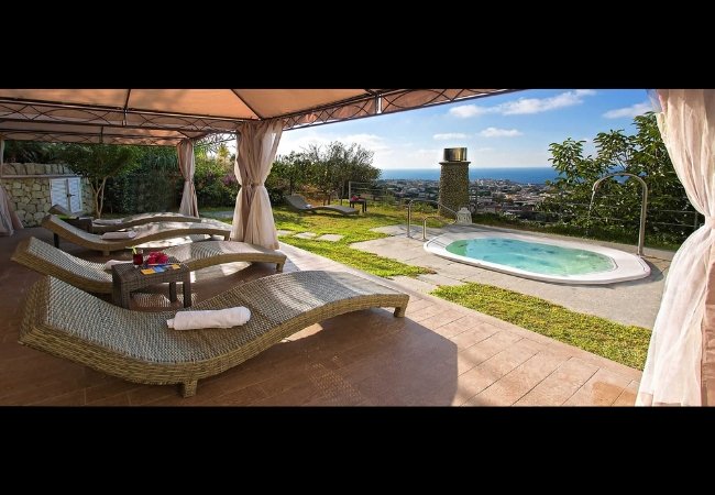 Zona relax con jacuzzi all'aperto, lettini e vista sul mare.