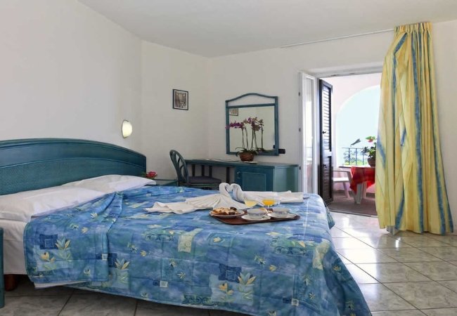 Camera da letto con letto matrimoniale azzurro, colazione su un vassoio e balcone.