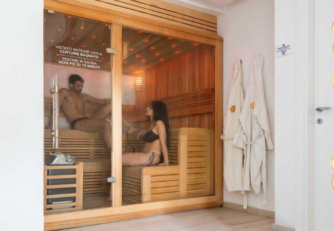 Due persone in un'accogliente sauna con luci soffuse e avvertenza sulla porta.