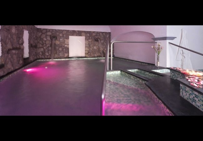 Piscina interna con luci rosa e scalini immersi.