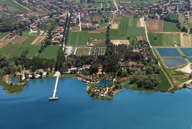 Vista aerea di un'area rurale con campi, edifici e un lago con un pontile bianco.