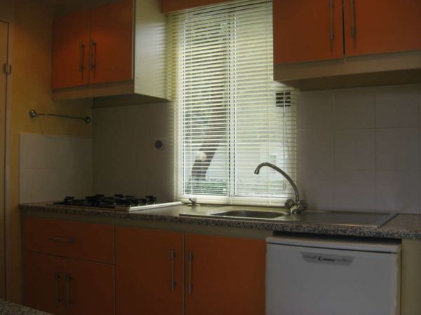 Cucina con fornelli a gas, lavandino, pensili arancioni e finestra con tende veneziane.