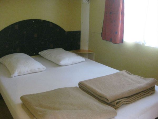 Camera da letto con letto matrimoniale, cuscini, coperte piegate e tenda rossa.