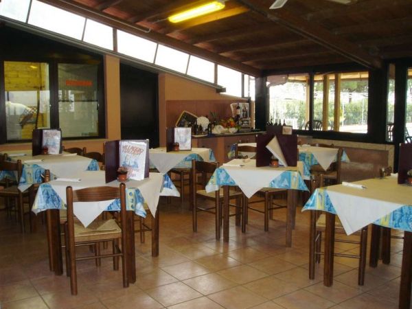 Una sala da pranzo con tavoli apparecchiati, sedie in legno e tovaglie a fantasia blu.