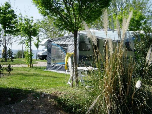 Una roulotte con veranda tra alberi e piante verdi in un campeggio.