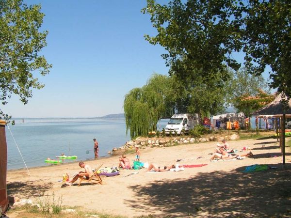 Spiaggia soleggiata con persone che prendono il sole, vista su un lago.