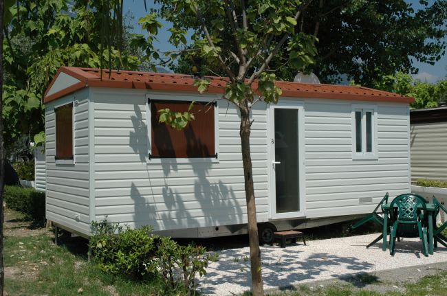 Casa mobile bianca con giardino e sedie verdi.