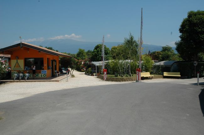 Vista di un campeggio con una casetta arancione, e vialetti con piante e cespugli.