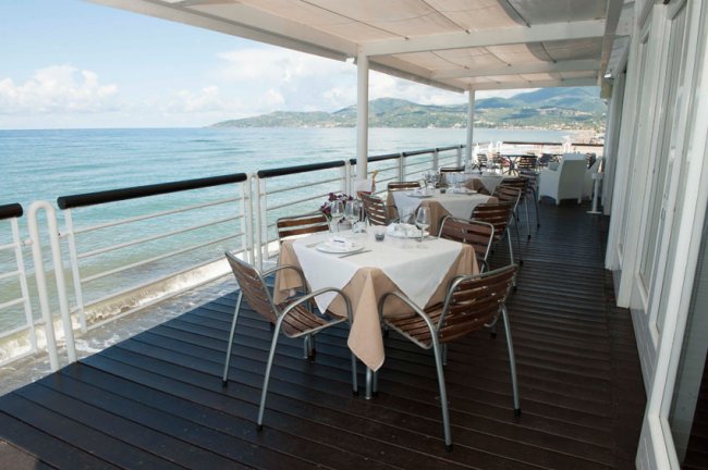 Tavoli apparecchiati su terrazza con vista mare.