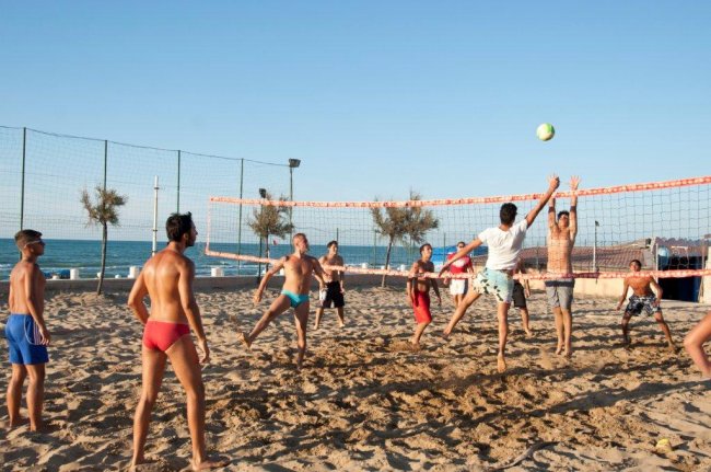 Persone giocano a beach volley su una spiaggia soleggiata.